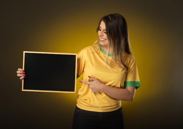 Braziliaanse fan met een schoolbord Vrouw fan viert in voetbal of voetbalwedstrijd op gele achtergrond Brazilië kleuren