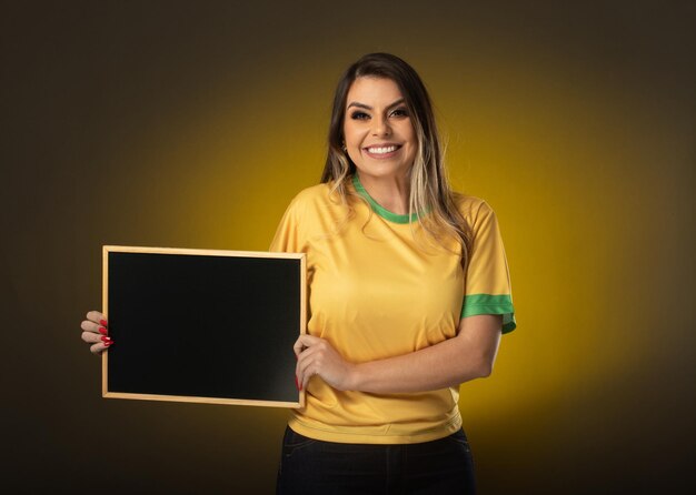 Braziliaanse fan met een schoolbord Vrouw fan viert in voetbal of voetbalwedstrijd op gele achtergrond Brazilië kleuren