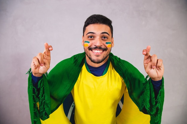 Braziliaanse fan met een vlag op hun rug juichen met hun vingers gekruist voor Brazilië om te winnen