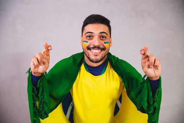 Braziliaanse fan met een vlag op hun rug juichen met hun vingers gekruist voor brazilië om te winnen