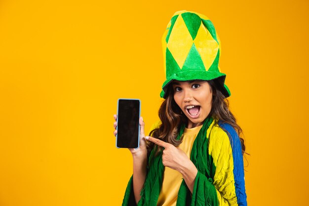 Braziliaanse fan. portret, braziliaanse fan die haar mobiele telefoon toont, verkleed als voetbalfan of voetbalwedstrijd op gele achtergrond. kleuren van brazilië.world cup