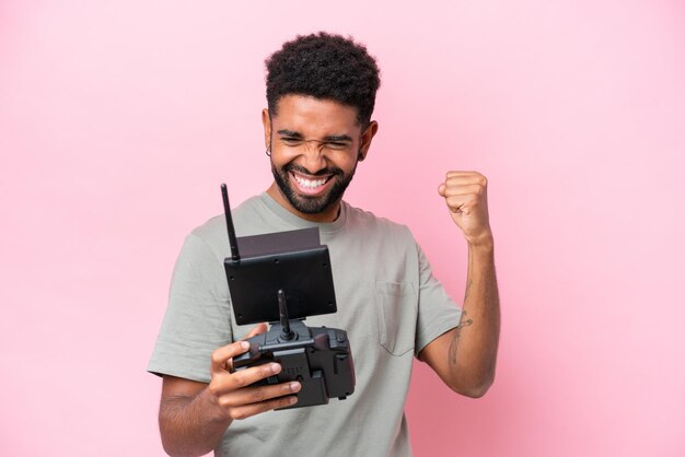 Braziliaanse man met een drone-afstandsbediening geïsoleerd op een roze achtergrond die een overwinning viert