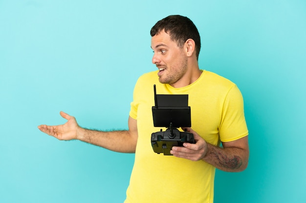 Braziliaanse man met een drone-afstandsbediening over een geïsoleerde blauwe achtergrond met een verbaasde uitdrukking terwijl hij opzij kijkt