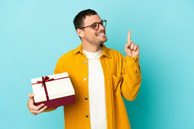 Braziliaanse man met een geschenk over een geïsoleerde blauwe achtergrond die een geweldig idee benadrukt