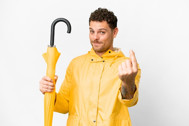 Braziliaanse man met regenbestendige jas en paraplu over geïsoleerde witte achtergrond die geldgebaar maakt