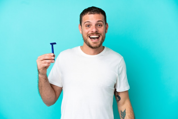 Braziliaanse man scheert zijn baard geïsoleerd op blauwe achtergrond met verrassende gezichtsuitdrukking