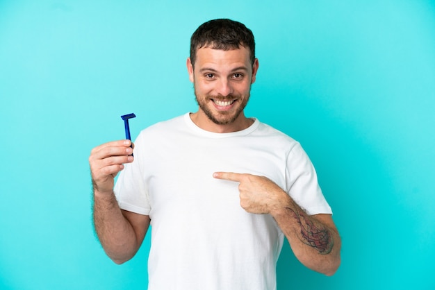 Braziliaanse man scheert zijn baard geïsoleerd op blauwe achtergrond met verrassende gezichtsuitdrukking