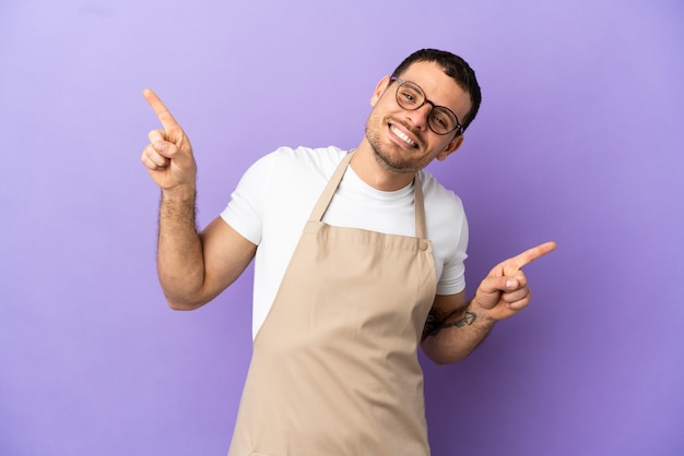 Braziliaanse restaurantkelner over geïsoleerde paarse achtergrond wijzende vinger naar de zijkanten en gelukkig?