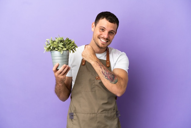 Braziliaanse tuinman die een plant vasthoudt over een geïsoleerde paarse achtergrond die een overwinning viert