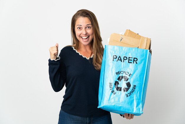 Braziliaanse vrouw van middelbare leeftijd die een recyclingzak vol papier houdt om over geïsoleerd te recyclen en een overwinning in winnaarspositie viert
