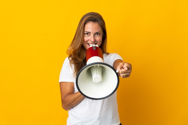 Braziliaanse vrouw van middelbare leeftijd geïsoleerd op geel schreeuwen door een megafoon om iets aan te kondigen terwijl ze naar voren wijst