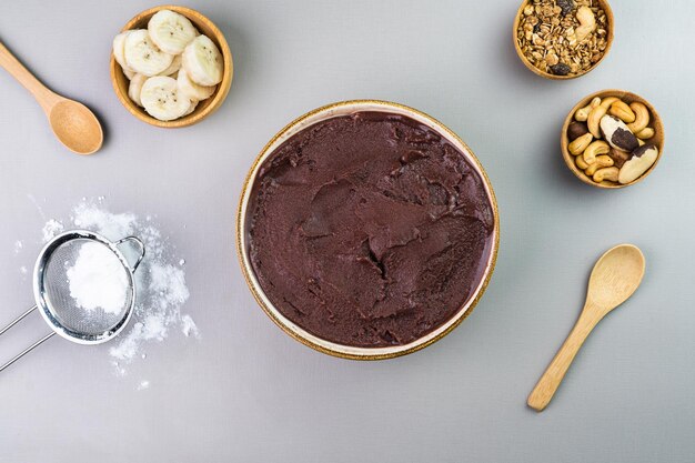 Brazilian acai in a white bowl additional banana granola and nuts in small bamboo bowls Cashew and Para nuts Top view Gray background Selective focus