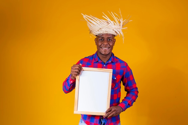 Brazilian afro man wearing typical clothes for the festa junina holding sign with space for text