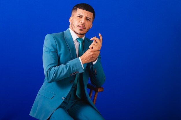 Brazilian black man dressed in a suit and blue tie business man wooden chair poses