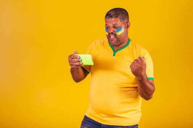 Brazilian black man soccer fan from brazil watching game on mobile smartphone