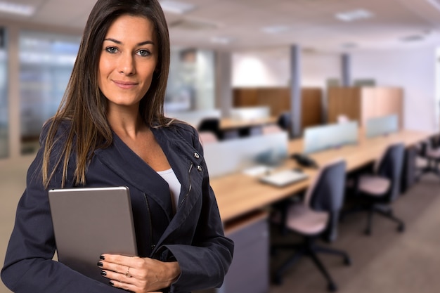 Brazilian business woman with tablet looking at camera in blurry office space. Copy space.