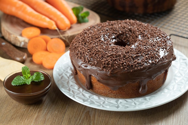 Brazilian carrot cake with chocolate frosting on wooden table with carrots in the background