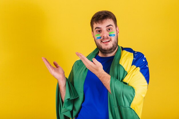 Brazilian caucasian man soccer fan from brazil pointing hands some product to left photo for ad indicating