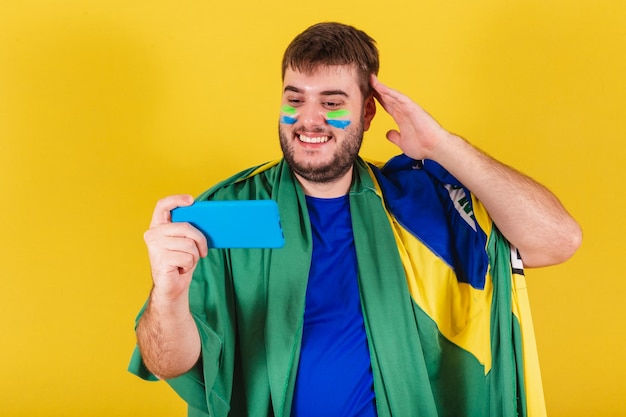 Brazilian caucasian man soccer fan from brazil watching soccer\
match by smartphone cellphone