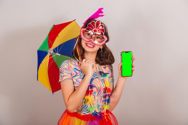 カーニバルの服を着たブラジルの子供の女の子がスマートフォンの緑色のクロマ画面を表示