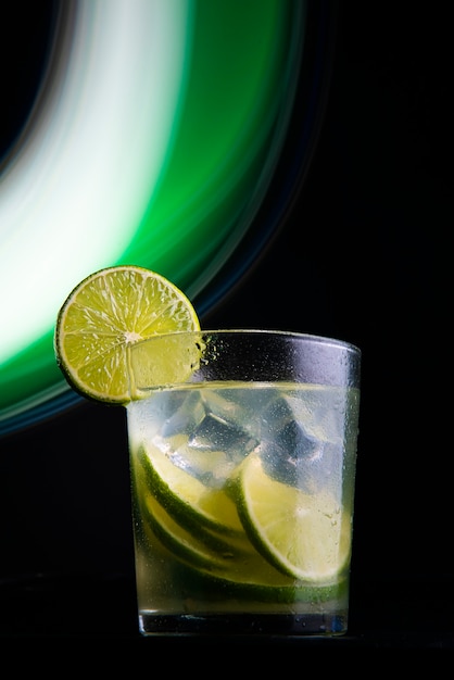 Cocktail brasiliano chiamato caipirinha. con limone, ghiaccio e cachaça su fondo scuro con luci colorate. copia spazio