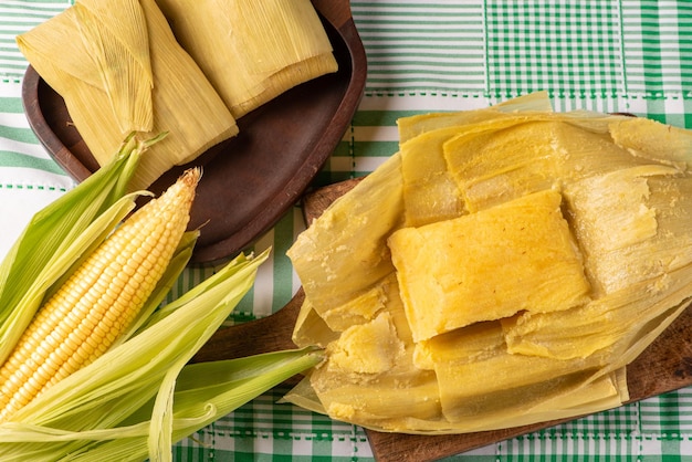 Photo brazilian corn snack pamonha and cornflower arranged on a table with green and white tablecloth top view