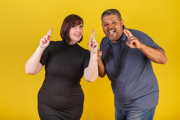 Photo brazilian couple caucasian woman and black man fingers crossed cheering wishing you a lot of luck sign