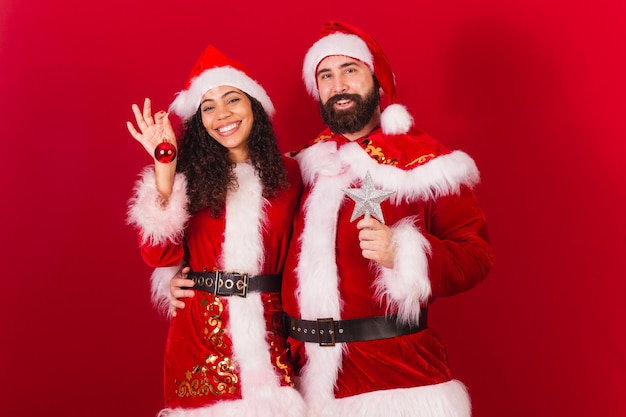 Brazilian couple dressed for christmas santa claus mummy claus holding christmas decoration star approved black woman and caucasian man