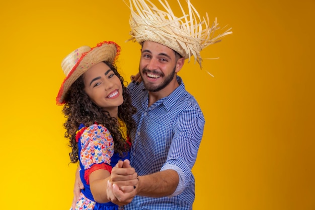 Brazilian couple wearing traditional clothes for Festa Junina dancing on yellow background