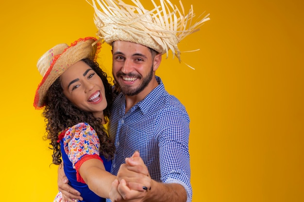 Brazilian couple wearing traditional clothes for Festa Junina dancing on yellow background