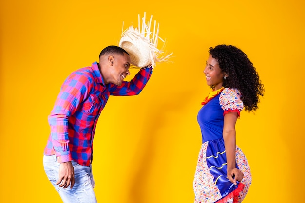 Brazilian couple wearing traditional clothes for Festa Junina dancing on yellow background