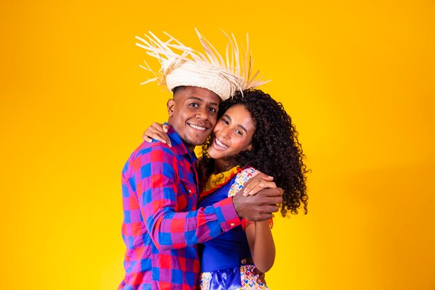 Brazilian couple wearing traditional clothes for Festa Junina dancing on yellow background