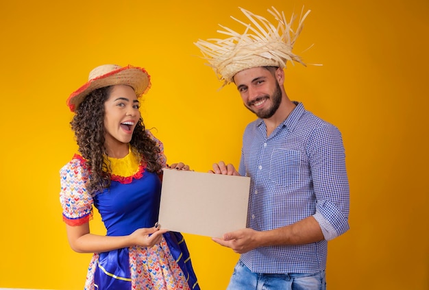 Brazilian couple wearing traditional clothes for Festa Junina holding a sign with copy space