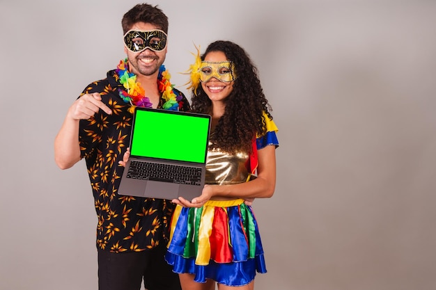 Brazilian couple with carnival clothes of holding notebook programming web