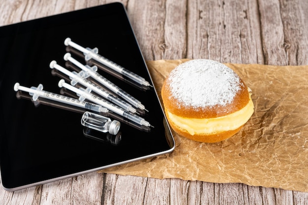 Brazilian cream donuts next by several syringes and ampoules with insulin on the tablet