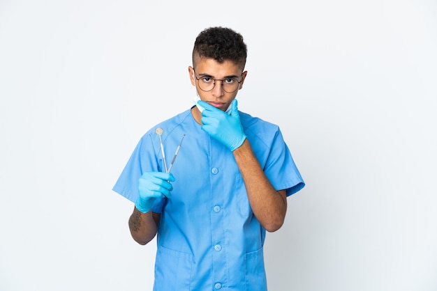 Brazilian dentist holding tool isolated on white wall thinking