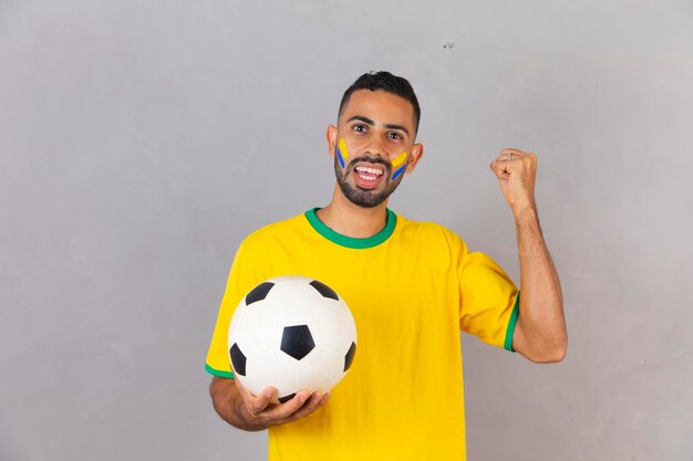 Brazilian fan on gray background celebrating victory holding a soccer ball