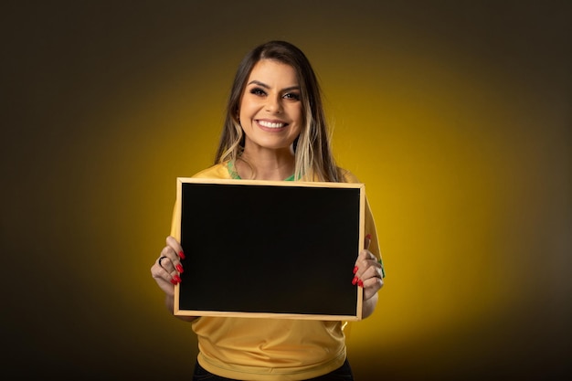 黒板を保持しているブラジルのファン 黄色の背景にサッカーまたはサッカーの試合で祝う女性ファン ブラジルの色