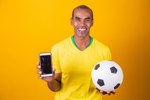 Brazilian fan man holding a smartphone with blank screen on yellow background