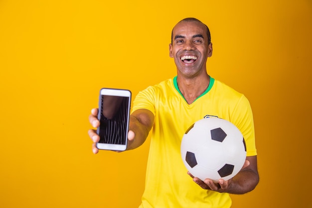 黄色の背景に空白の画面でスマートフォンを保持しているブラジルのファンの男
