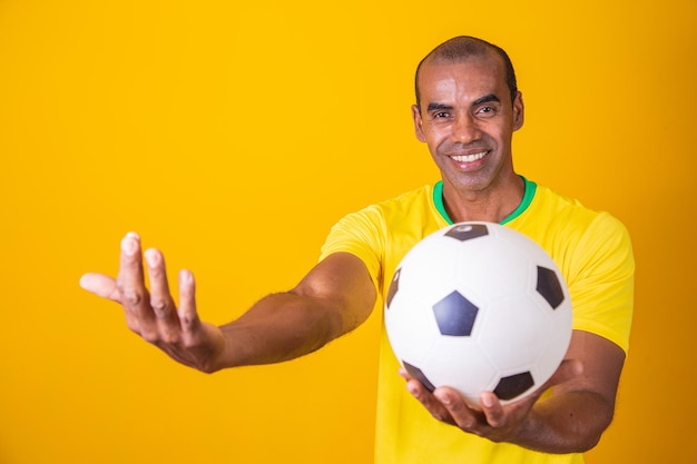 Brazilian fan man holding soccer ball with copy space on yellow background