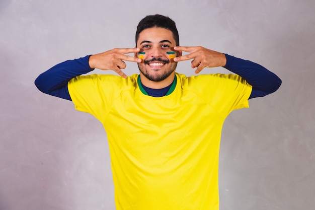 Brazilian fan. using paint as makeup, Brazilian fan celebrating football or soccer game on grey background. Colors of Brazil.