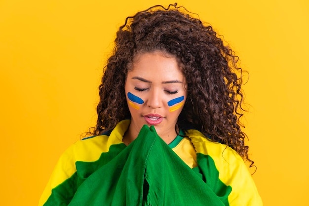 Brazilian fan with flag praying on yellow background praying for brazil