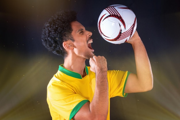 Giocatore nero di calcio brasiliano che tiene palla e festeggia