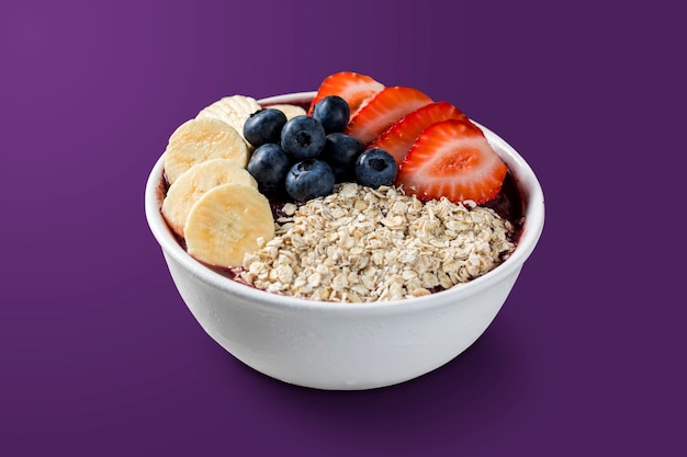 Brazilian frozen aÃ§ai berry ice cream bowl with strawberries, bananas, blueberry and granola. isolated on purple background. Summer menu front view.