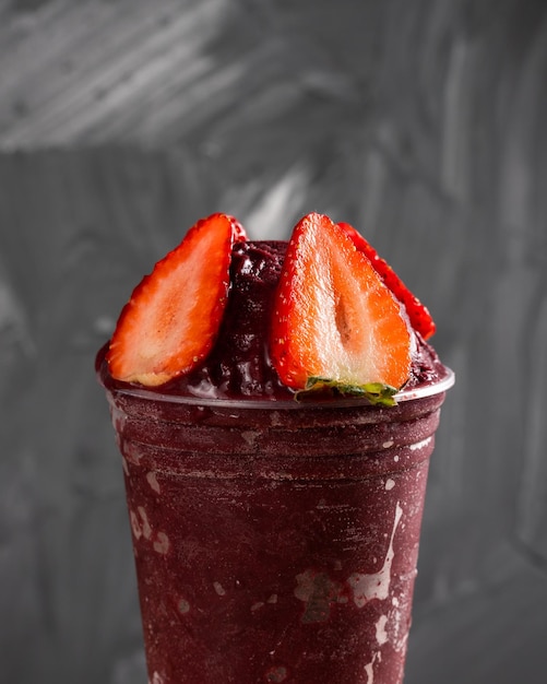 Brazilian Frozen AÃ§ai Berry Ice Cream Smoothie in plastic cup with Strawberries. On a wooden desk and a gray summer background. Front view for menu and social media