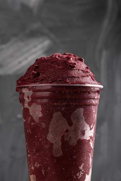 Brazilian Frozen AÃ§ai Berry Ice Cream Smoothie in plastic cup. On a wooden desk and a gray summer background. Front view for menu and social media