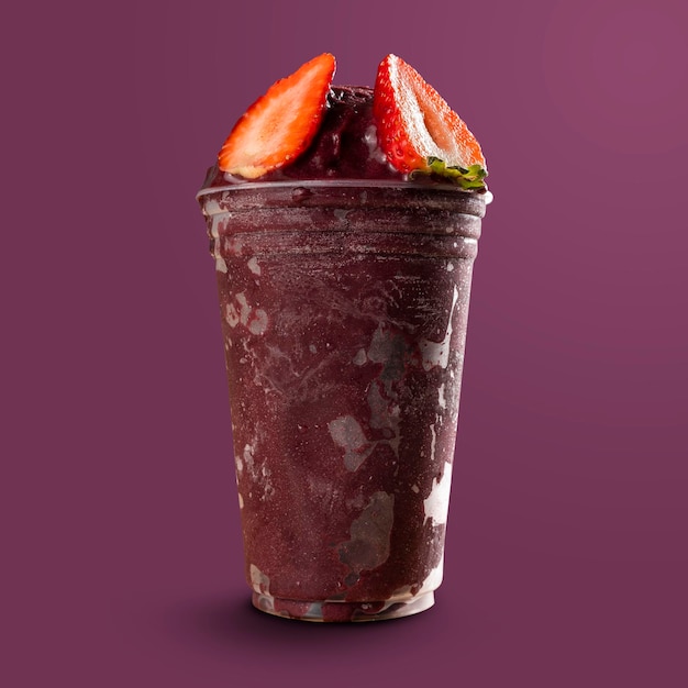 Frullato di gelato alla bacca di açai congelato brasiliano in tazza di plastica con fragola. isolato su sfondo viola. vista frontale per menu e social media