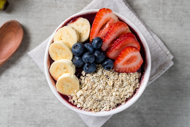 Brazilian frozen and acai berry ice cream bowl with strawberries, bananas, blueberry and oatmeal flakes. with fruits on wooden background. Summer menu top view. close up.