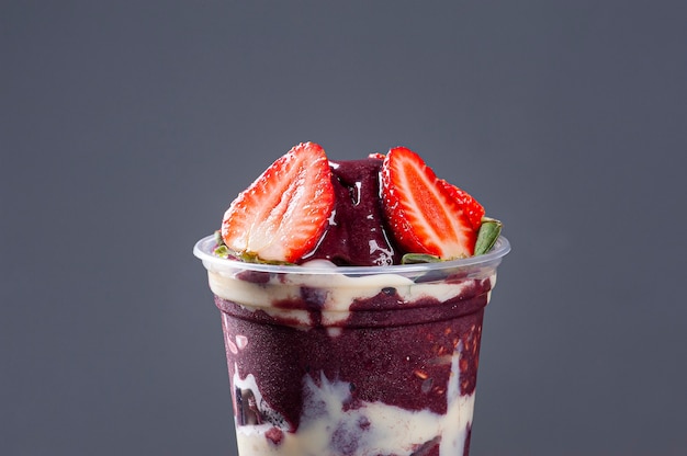 Brazilian frozen açaí­ in a plastic cup with condensed milk and strawberry. Fruit from the Amazon.